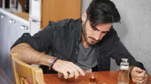 Young man sitting drinking alone at a table with two bottles of liquor Stock Photos