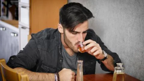 Young man sitting drinking alone at a table with two bottles of liquor Stock Photos