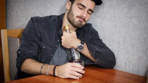 Young man sitting drinking alone at a table with two bottles of liquor Stock Photos