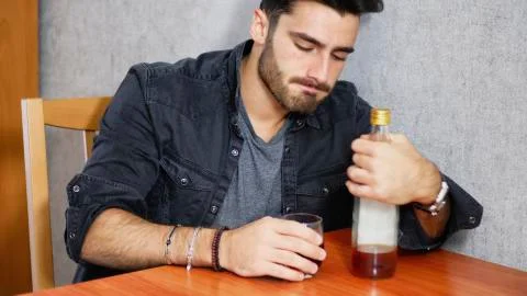 Young man sitting drinking alone at a table with two bottles of liquor Stock Photos
