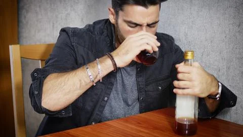Young man sitting drinking alone at a table with two bottles of liquor Stock Photos