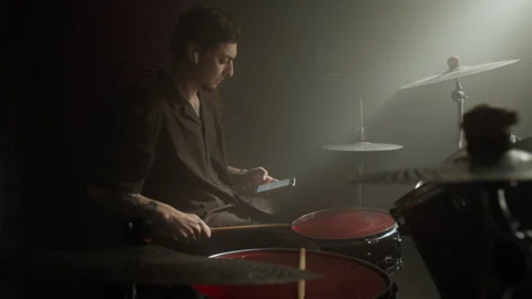Young Man Sitting at Drum Kit Using Smartphone in Recording Studio Stock Footage 338399123