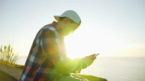 Young man sitting on the edge of a cliff using a smartphone Stock Footage 146631815