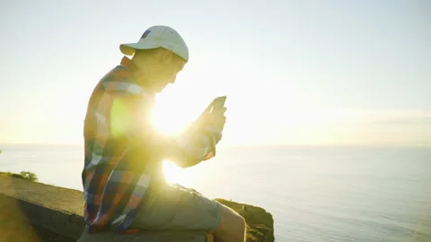 Young man sitting on the edge of a cliff using a smartphone Stock Footage 146631857