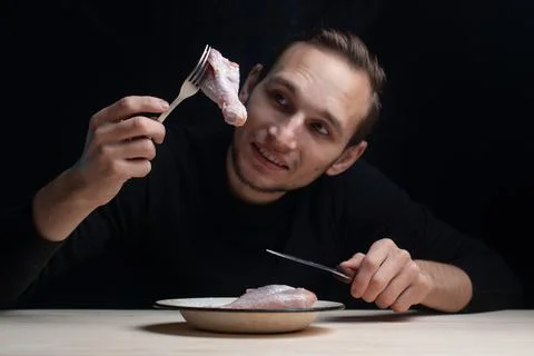 A young man is sitting at an empty table with a plate of raw chicken on it, the Stock Photos
