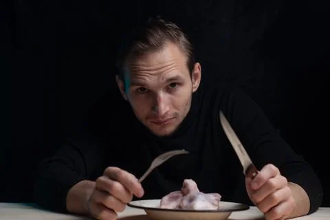A young man is sitting at an empty table with a plate of raw chicken on it, the Stock-Fotos