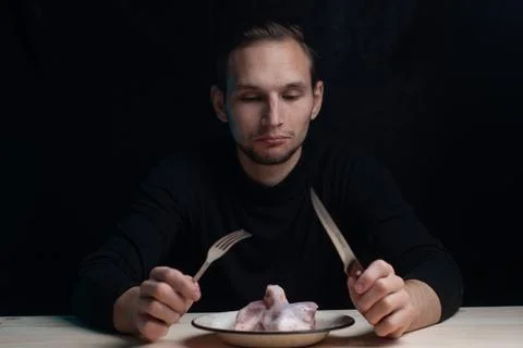 A young man is sitting at an empty table with a plate of raw chicken on it, the Stock Photos