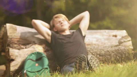 Young man sitting by the fallen tree's stem and resting in the sun Stock-Footage 60605040