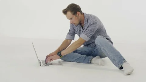 Young man sitting on the floor and typing  on a laptop on white background. 動画素材 80349617