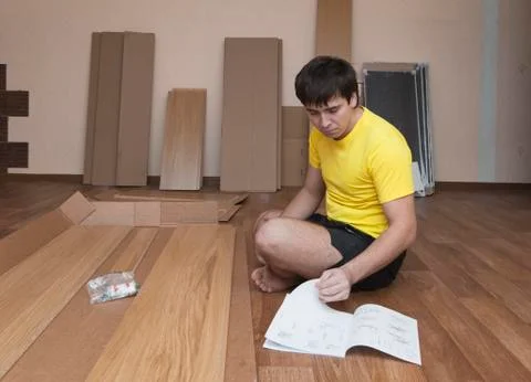 Young man sitting on floor assembling flatpack closet Stock Photos