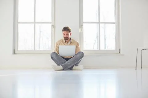 Young man sitting on floor browsing laptop in empty new home 스톡 사진