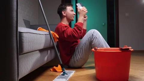 Young man sitting on the floor, laughing and watching a video on his Stock Footage 342771236