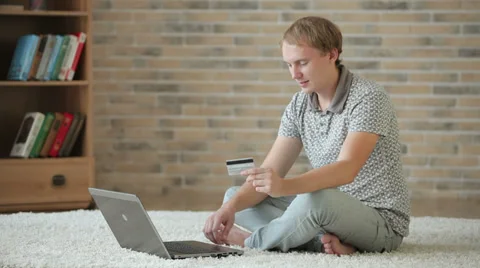 Young man sitting on floor using laptop holding credit card looking at camera Stock Footage 34278400
