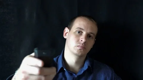 Young man sitting in front of the camera and switches the channels,watching TV Video stock 76545325