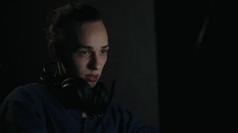 Young man sitting in front of computer at home in dark room Видео 99051304