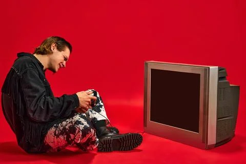 Young man sitting in front of retro TV with blank screen and trying to play Stock Photos