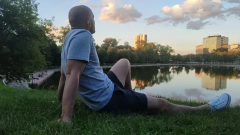 Young man sitting on grass and admiring view of lake Stock Footage 202610459