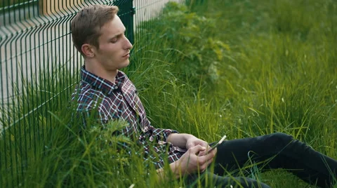 Young man sitting on the grass with cellphone Stock Footage 64683977
