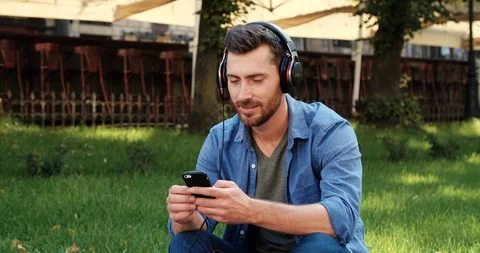 Young Man is sitting on the grass in park and listening to music in Headphones Stock Footage 111466541