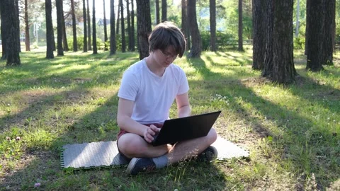 Young man is sitting on the grass in park with his laptop Stock Footage 136236622
