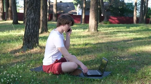 Young man is sitting on the grass in park with his laptop Stock Footage 136237002