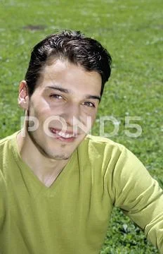 Young man sitting on grass, portrait, close-up Stock Photos