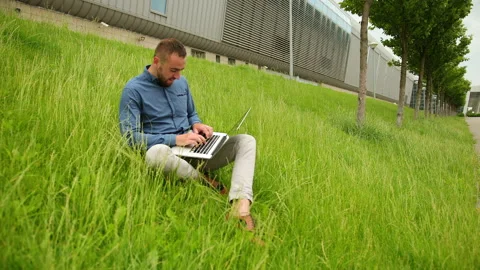 Young man sitting on grass, using laptop, male with computer running remotely Stock-Footage 135151417