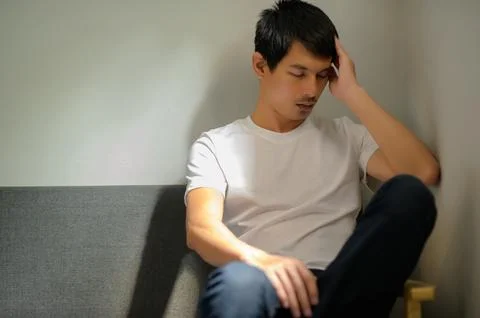 Young Man Sitting in a Gray Couch with Contemplative Expression Stock Photos