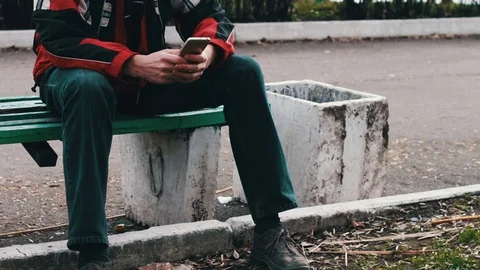 Young man is sitting on a green bench in the park waiting for someone else and Stock Footage