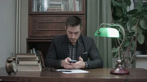 Young man sitting at his study table with books and using mobile phone Vídeos de archivo 73686289