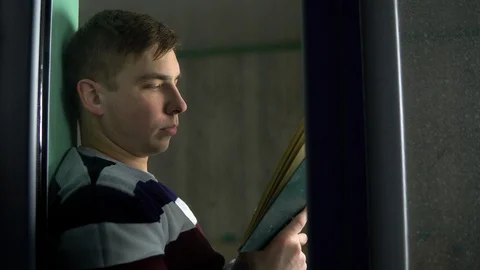 A young man is sitting at home with a book in his hands. A man sits on a window Stock-Footage 129408093
