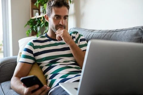 Young man sitting at home using a laptop and cellphone Stock Photos