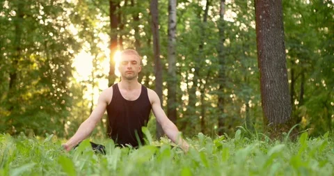 Young man sitting on lawn doing meditation in city park. Men sitting on grass in Stock Footage 156522713
