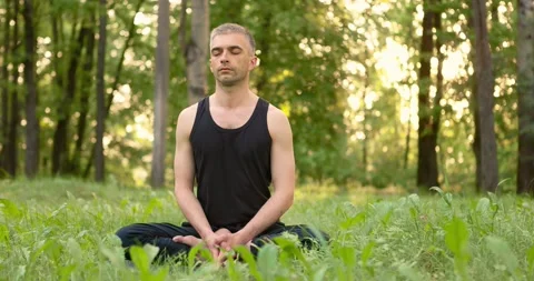 Young man sitting on lawn doing meditation in city park. Men sitting on grass in Stock Footage 156525505