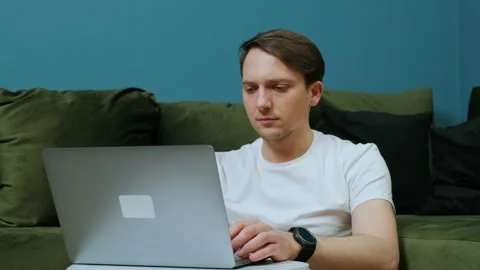 Young man sitting near sofa with laptop, working from home concept. Stock Footage 148658352