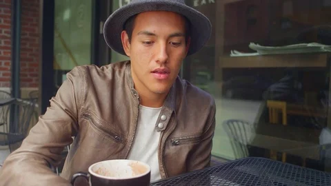 Young man sitting outside a coffee shop smiles and drinks his coffee Stock Footage