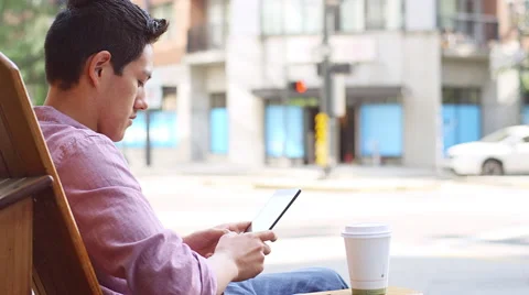 A young man sitting outside using his tablet and drinking coffee Stock Footage 57511624
