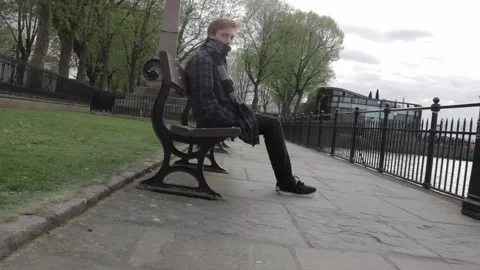 Young Man Sitting on Park Bench Along the Thames River in Greenwich, London Stock Footage 335124575