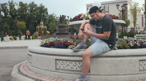 Young Man Sitting In The Park Looking At Smartphone And Smiling. Slow-Mo. Video stock 65039346