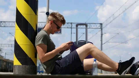 Young man sitting on the platform and having fun while playing games  smartphone Stock Footage 78650798