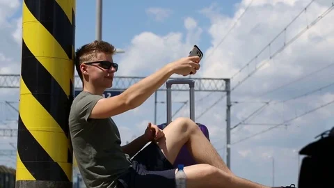 Young man sitting on the platform and doing selfies on smartphone Stock Footage 78651296
