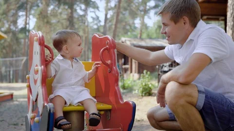 Young man sitting in playground with son on swing Stock Footage 95031553