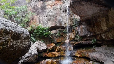 Young man sitting on the rock under tropical waterfall. Stock Footage 125030673