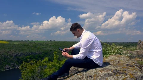 Young man sitting on a rock using a mobile Stock-Footage 108114348