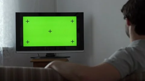 Young man sitting on a sofa and watching TV with green screen. Stock Footage 150827228