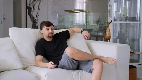 Young man sitting on the sofa and turning on the television. Video stock 247660891