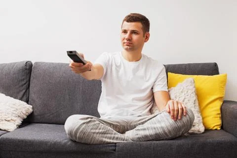 Young man sitting on sofa and holding tv remote control Stock Photos
