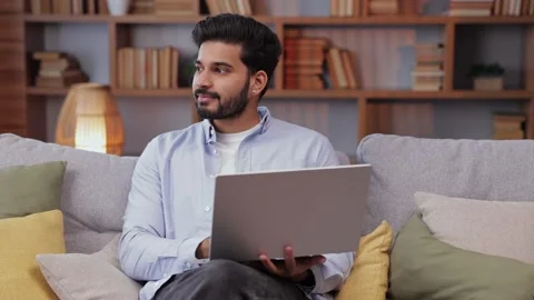 Young man sitting on sofa couch in living room. Indian millenial guy browsing Video stock 238541259