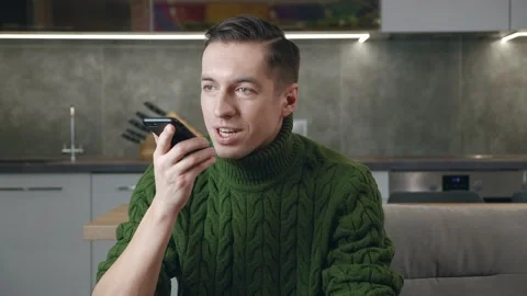 Young man sitting on sofa holding smartphone calling using speaker phone Stock Footage 197357976