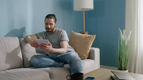 Young Man Is Sitting On Sofa at Home, Communicating Online Vídeo Stock 129892434
